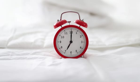 Red alarm clock on white bed linen, close-up. Wake me up hotel concept, morning sleep, bedtime