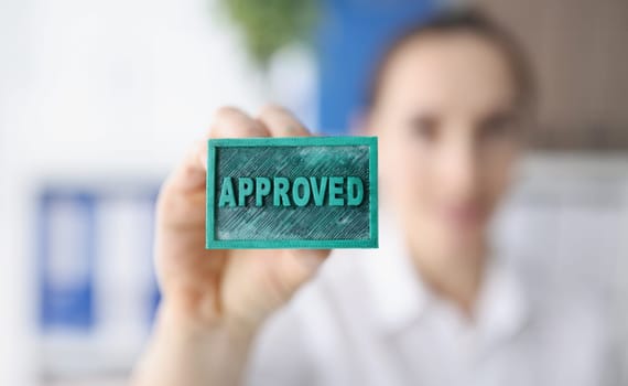 A woman holds a stamp inscription approved, close-up, blurry. Approval, labeling of documents, concept verification