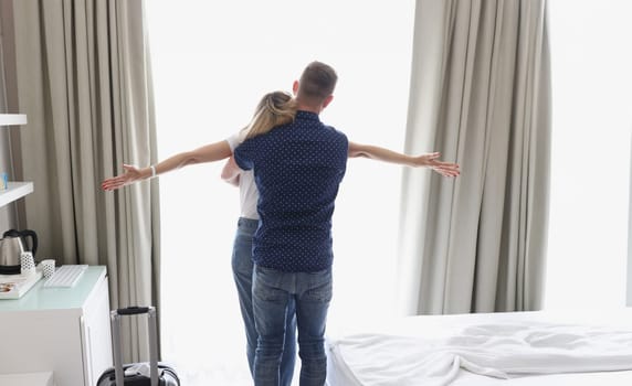 In a hotel at the window, a man hugs a woman, rear view. Family adventure, vacation. Accommodation booking