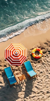 Aerial shot of a sunny beach scene with colorful umbrella, lounge chairs, and a lifebuoy on the sand.