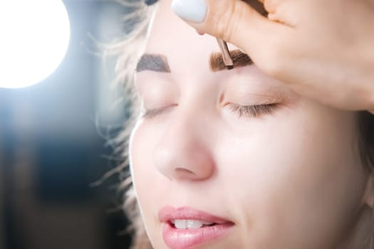 Eyebrow tinting. Close-up of a master applying eyebrow dye with a brush. Cosmetic procedures, permanent eyebrow makeup. correction and modeling of eyebrows in a beauty salon. perfect eyebrows.