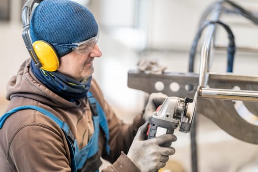 A worker in workwear, including ear muffs and a beanie, is operating machinery to manipulate a piece of metal in an engineering job