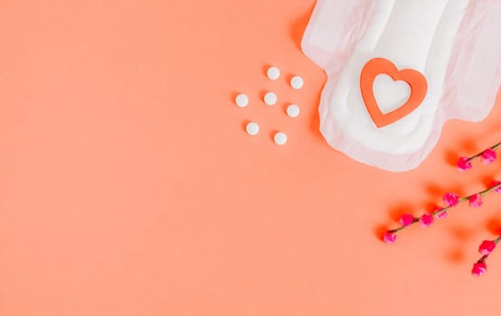 One open white female pillow with one red wooden heart, tablets and willow branches lie on the right on a peach-pink background with a copy space on the left, flat lay close-up.