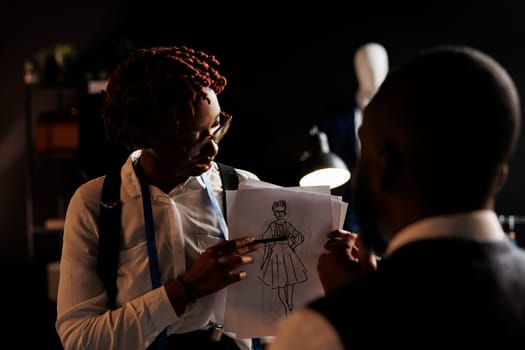 Experienced fashion designer showing couturier sketch drawing of wedding dress she wants him to customize. African american dressmakers working on stylish bespoke sartorial attire