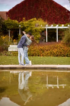 A couple in love hugs on the shore of a city pond in the European town. love story against the backdrop of autumn nature. romantic ambiance, couple goals, outdoor romance, seasonal charm, love in the city, autumnal vibes, European town, city pond, affectionate bonding, love story