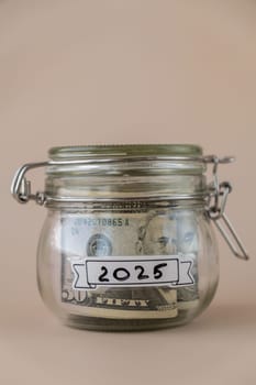 Glass jar full of American currency dollars cash banknote with text 2025 year. Preparation saving money. Moderate consumption and economy. Collecting money