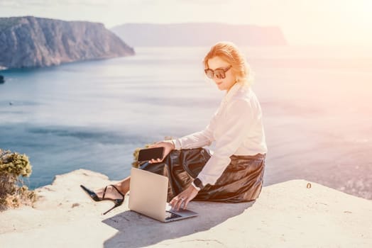 Digital nomad, Business woman working on laptop by the sea. Pretty lady typing on computer by the sea at sunset, makes a business transaction online from a distance. Freelance remote work on vacation