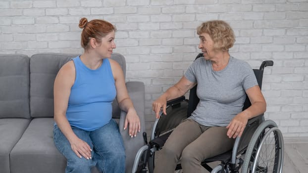 Elderly woman in wheelchair with pregnant daughter at home