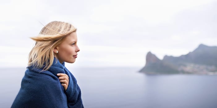 Thinking, ocean and woman with blanket in nature for adventure on holiday, vacation and weekend outdoors. Mountain, travel and person by seaside for relaxing, happiness and peace in countryside.