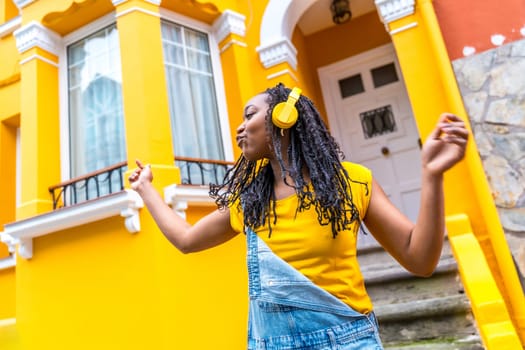 Low angle view portrait of a happy african woman dancing listening to music with headphones outside a yellow house