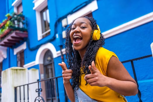 African woman gesturing dancing in the street listening to music next to a house with blue facade