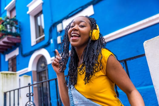 African woman singing to the camera and dancing in the street next to a blue house
