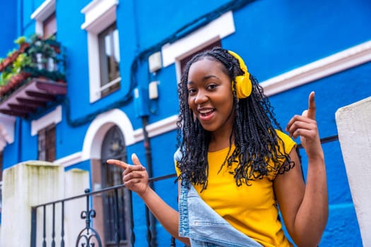 African woman singing while listening to music with headphones standing in a street with blue colored houses