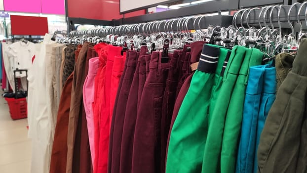 Row of different colorful pants trousers on hanger in shop. Close up