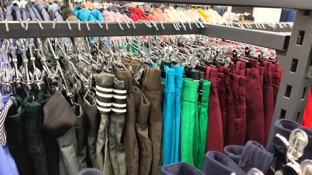 Row of different colorful pants trousers on metall hanger in shop. Close up