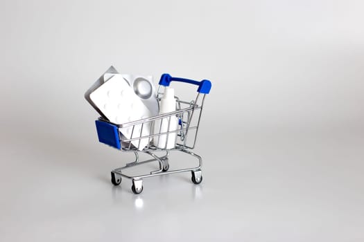 White and silver blisters of pills and drops in a small supermarket trolley on a white background. Copy space