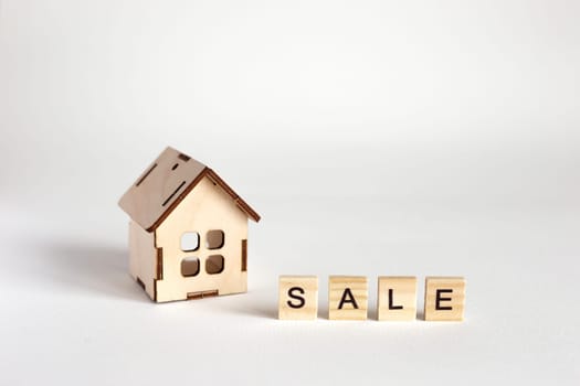 A small wooden toy house, stands on a white background and an inscription from wooden letters Sale. Copy space. Close up