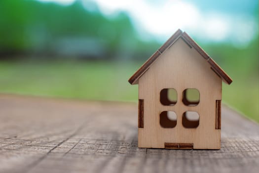 small wooden toy house stand on a wooden table on the background of green spring nature. Copy space. Close up