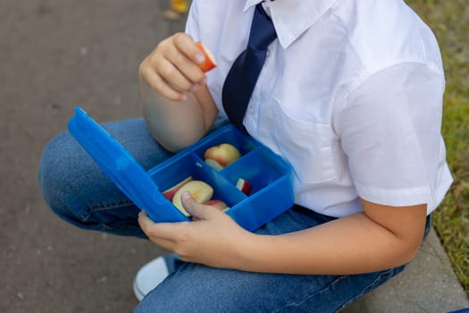 Schoolboy in white shirt with blue tie holding blue lunch box with apples. No face. Close up