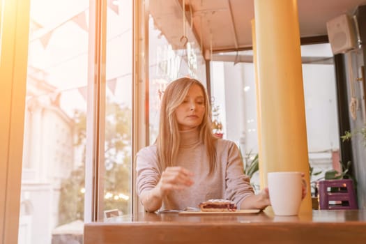 Woman with blonde hair sips cappuccino in a cafe. She is holding the glass up to her face, taking a sip of the drink