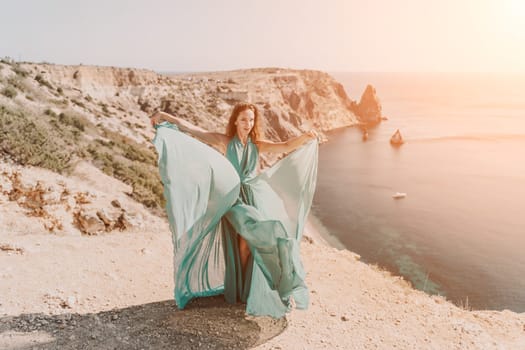 Woman green dress sea. Female dancer posing on a rocky outcrop high above the sea. Girl on the nature on blue sky background. Fashion photo