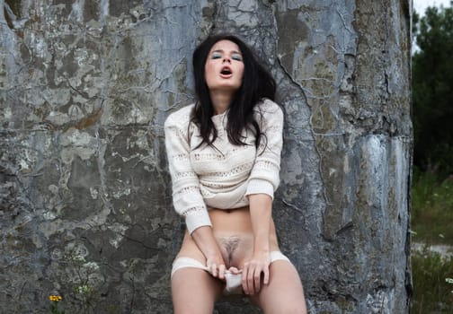 Young naked woman posing near a concrete wall