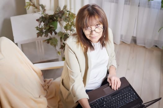 Elderly lady with glasses and laptop in room. Businesswoman is leader, manager working online. Blogger streaming. Grandma with family on Internet