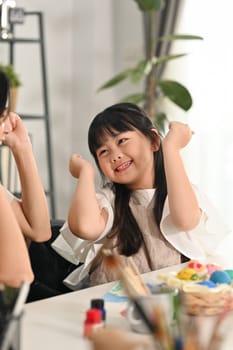 Cheerful little child girl painting eggs with mother, preparing for Easter holiday at home together.