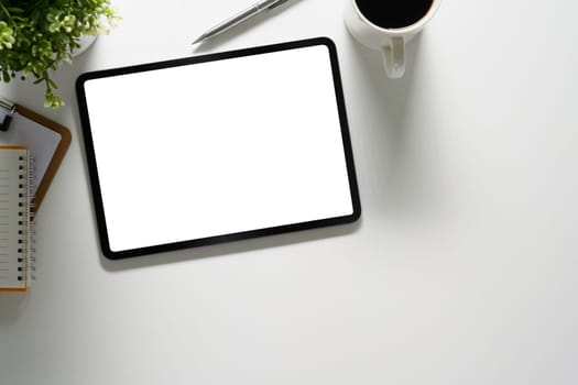 Digital tablet with empty screen, coffee cup and notepad on white table.