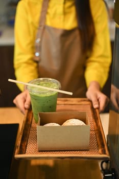 Female waitress in apron serving matcha green tea Choux cream puffs in a cardboard tray to customer.