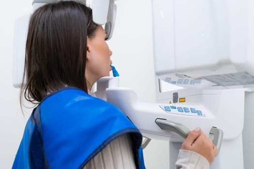 Young woman patient standing in x ray machine for panoramic radiography of teeth.