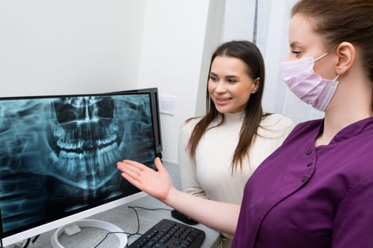 Dentist shows the X ray of teeth on the screen to the patient in the the clinic.
