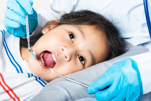 Dental kid health examination. Doctor examines oral cavity of little child uses mouth mirror to checking teeth cavity, Asian dentist making examination procedure for smiling cute little girl