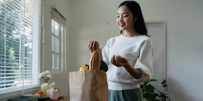 Organic Food Delivery. Happy young woman unpacking bag with Fresh Vegetables in kitchen.