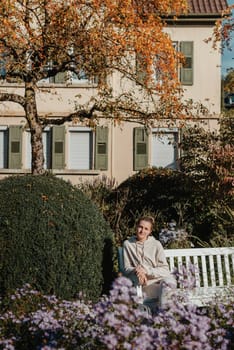 a girl sits on a bench in the park and enjoys the sun. Portrait young adult attractive woman enjoy sitting on bench and relaxing calm carefree rest in city park against green grass and trees on sunny day. Single female person relaxing chilling outdoors