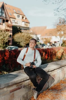 Man Sitting on Stairs in Old European City And Holding Photo Camera. Contemporary Stylish Blogger And Photographer