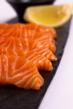 A close-up of a fresh salmon fillet garnished with lemon wedges and soy sauce on a black stone plate. This appetizing seafood dish is isolated on a white background, perfect for a healthy meal.