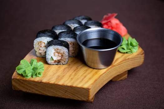 Sushi assortment featuring a variety of rolls and sashimi beautifully arranged on a wooden plate, accompanied by chopsticks and a side of savory soy sauce. Elegant presentation on a white background.