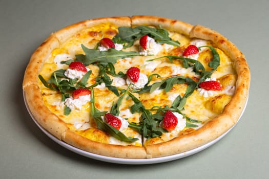 A delicious pizza with strawberries, cream cheese, and arugula on a white plate. The pizza is isolated on a green background. The pizza is perfect for a summer party or a picnic.