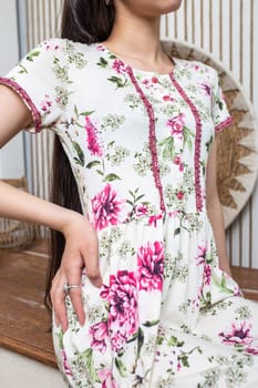 A young woman poses in a floral summer dress with pink flower buttons and intricate lace details. The relaxed silhouette and flared skirt add elegance, suitable for various occasions.