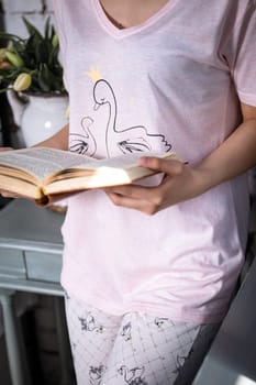 A young woman with long dark hair in a pink nightgown reading a book on a cozy bed. She looks serene and focused, surrounded by a soft pink background that exudes peace and tranquility.