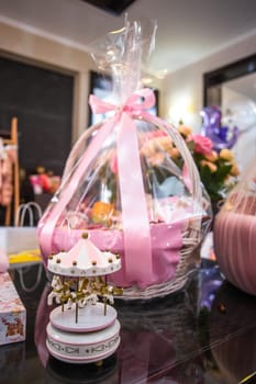 Elegant baby shower gift basket filled with essentials and toys, adorned with a pink bow and cute carousel. Perfect for invitations, announcements, or as a thoughtful gift guide item.