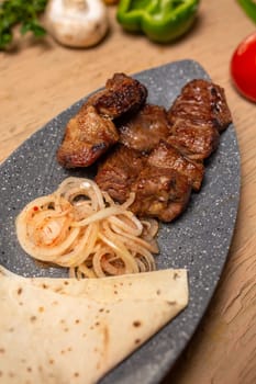 Grilled meat and vegetables on a rustic wooden table with soft flatbread. Succulent meat, tender veggies, vibrant tomatoes, peppers, mushrooms, onions create a delicious meal.