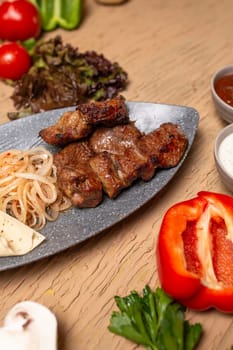 Plate of delicious Uzbek shish kebabs with marinated meat, grilled vegetables, and fresh herbs served on a rustic wooden table. Background is blurred, with vibrant colors and a top-down view.