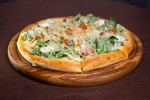 A delicious round pizza with salad, tomatoes, cheese, croutons on wooden board. Isolated on brown background, perfect for food blogs, restaurant websites, social media.