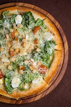 A delicious round pizza with salad, tomatoes, cheese, croutons on wooden board. Isolated on brown background, perfect for food blogs, restaurant websites, social media.