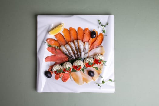 An artfully arranged platter of fresh seafood - salmon, trout, caviar, and shrimp - on a white plate with lemon slices and greens. A visually appealing still life composition.