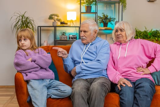 Irritated grandfather and grandmother scolding granddaughter for bad behavior and disobedience on couch raising voice, scream at little grandchild. Difficulties of upbringing, misbehaved child concept