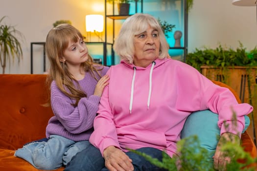 Loving worried kind girl granddaughter consoling sad crying grandmother helping with problem comforting talking to upset senior woman in tears, empathy support embracing sitting on sofa in living room