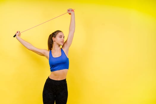 Portrait of gentle muscular woman holding skipping rope on her neck over yellow background